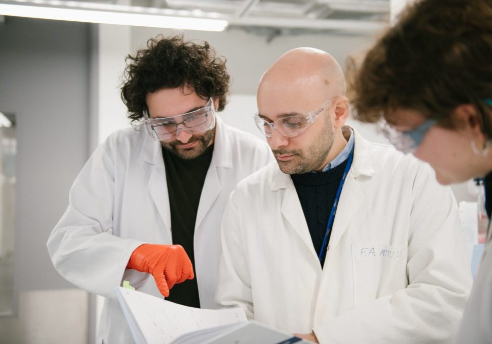 Three scientists wearing lab coats looking at something in a laboratory.